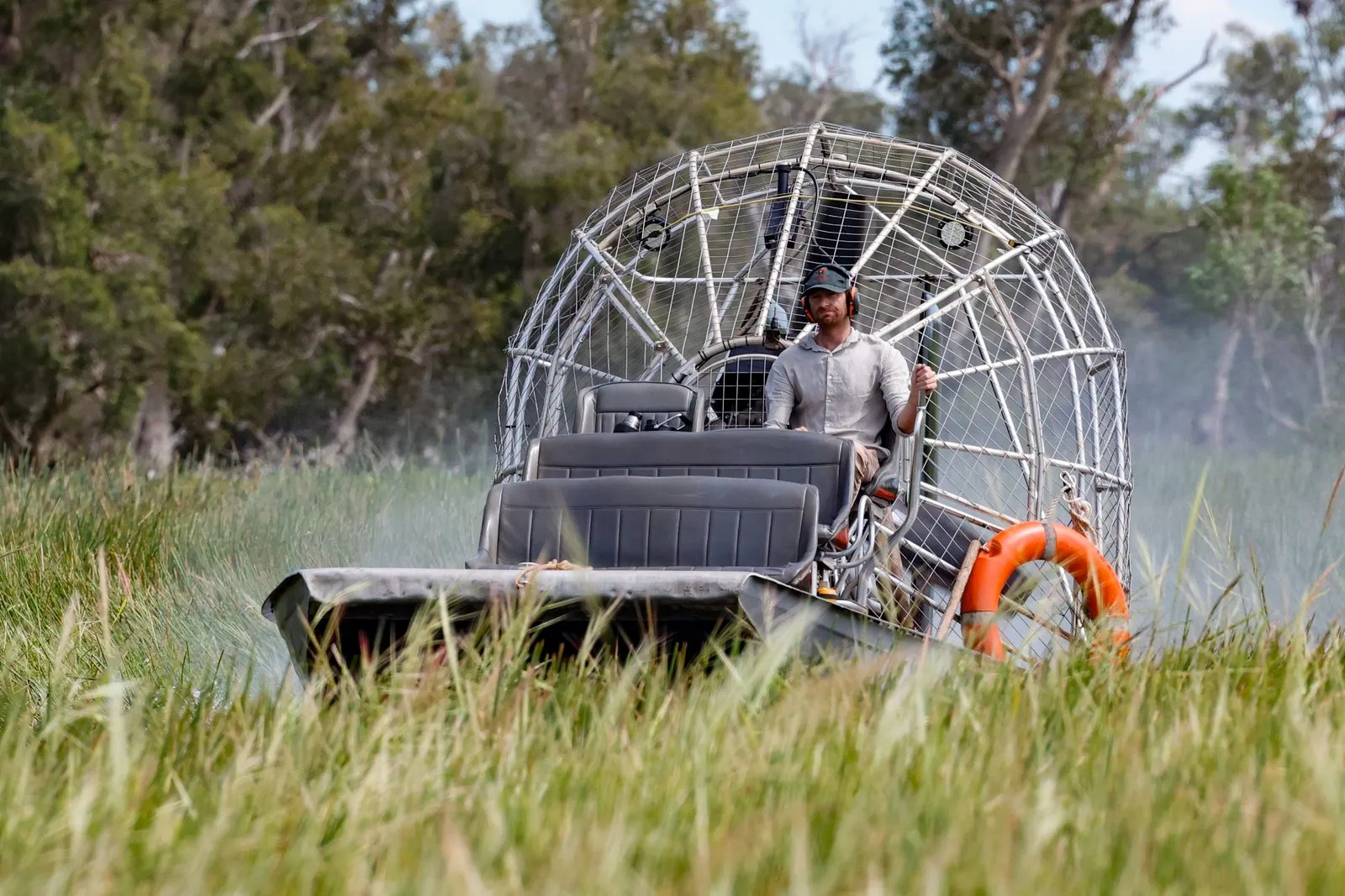 An operator at the controls of an airboat, pushing through tall grass on a Northern Territory wetland.