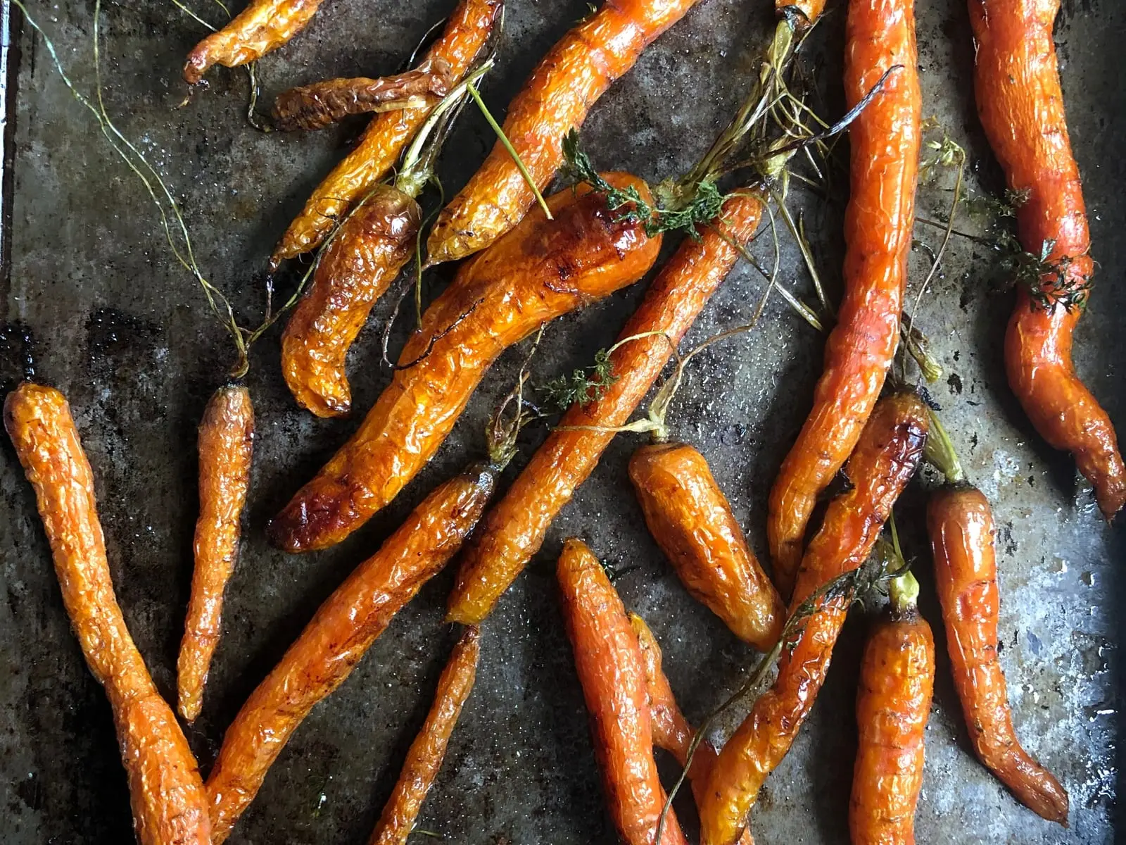 Whole baby carrots roasted with their tops, on a well-used baking tray.