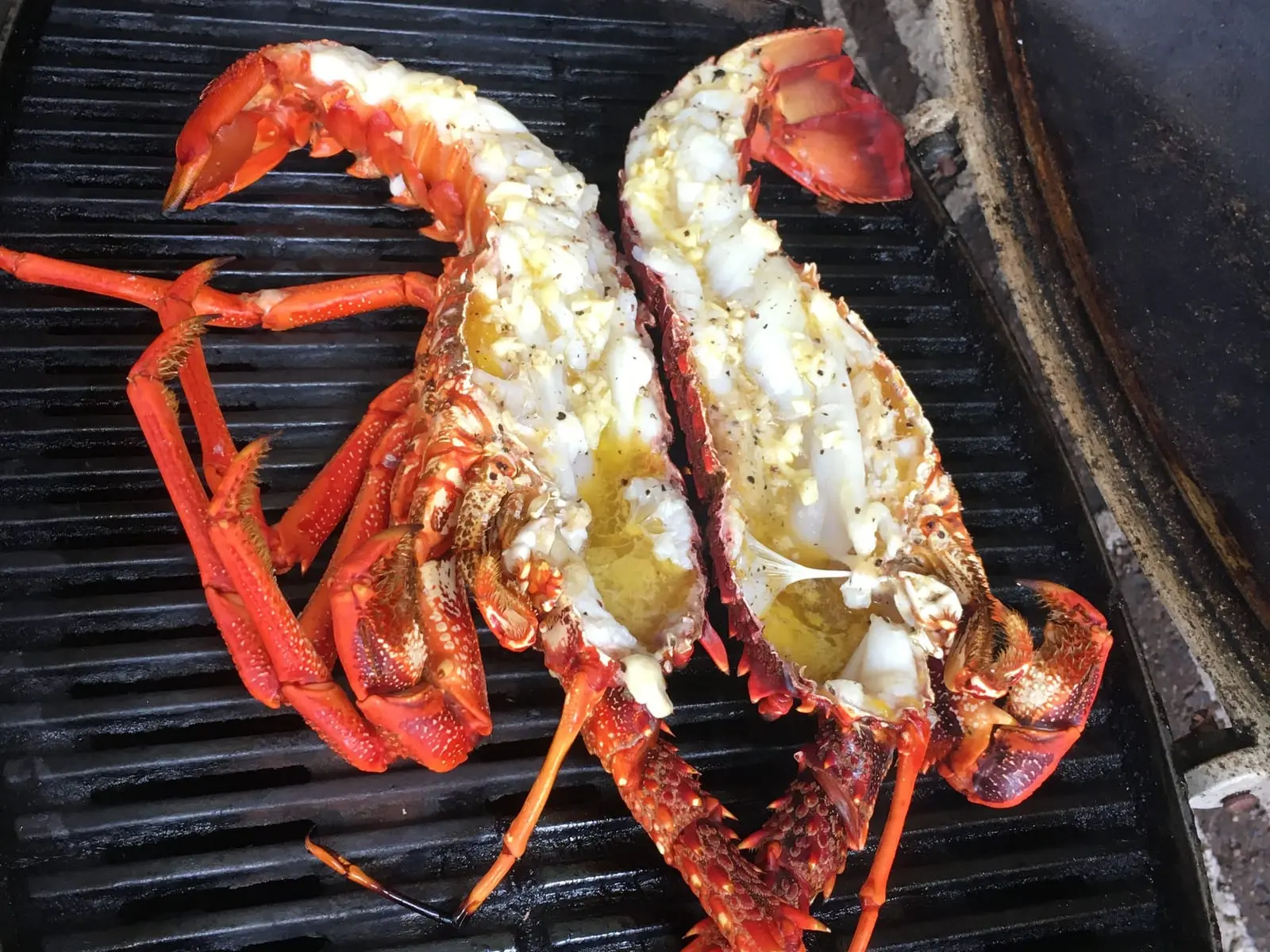 Two halves of a rock lobster brushed with garlic butter, cooking on a barbecue grill