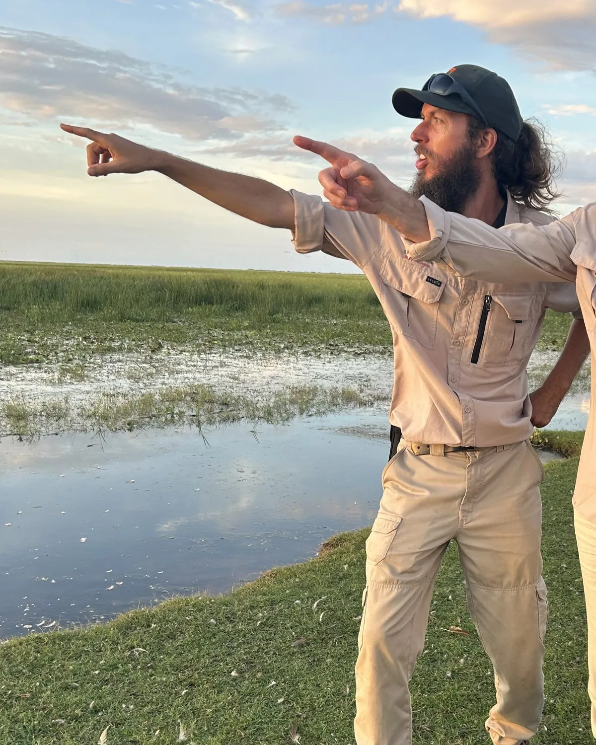 A guide on a Top End floodplain at dusk, pointing out across the water.