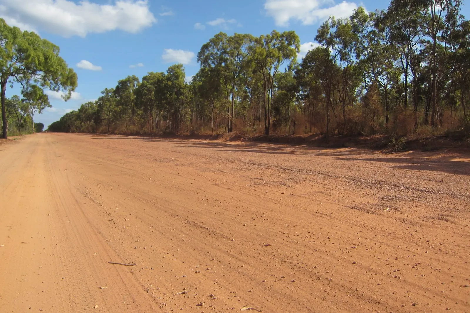 A wide red gravel road running through open savanna woodland under a blue sky, far north Queensland.